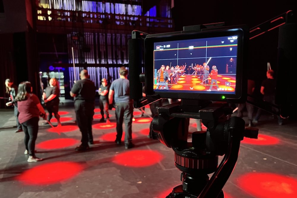 Action Lab Shot 3 Camera monitor framing a stage rehearsal with light sabers, performers scattered under red spotlights in the background